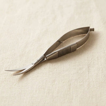 Curved micro spring scissors in satin stainless steel with ribbed finger grips and a sprung loop handle, on linen cloth