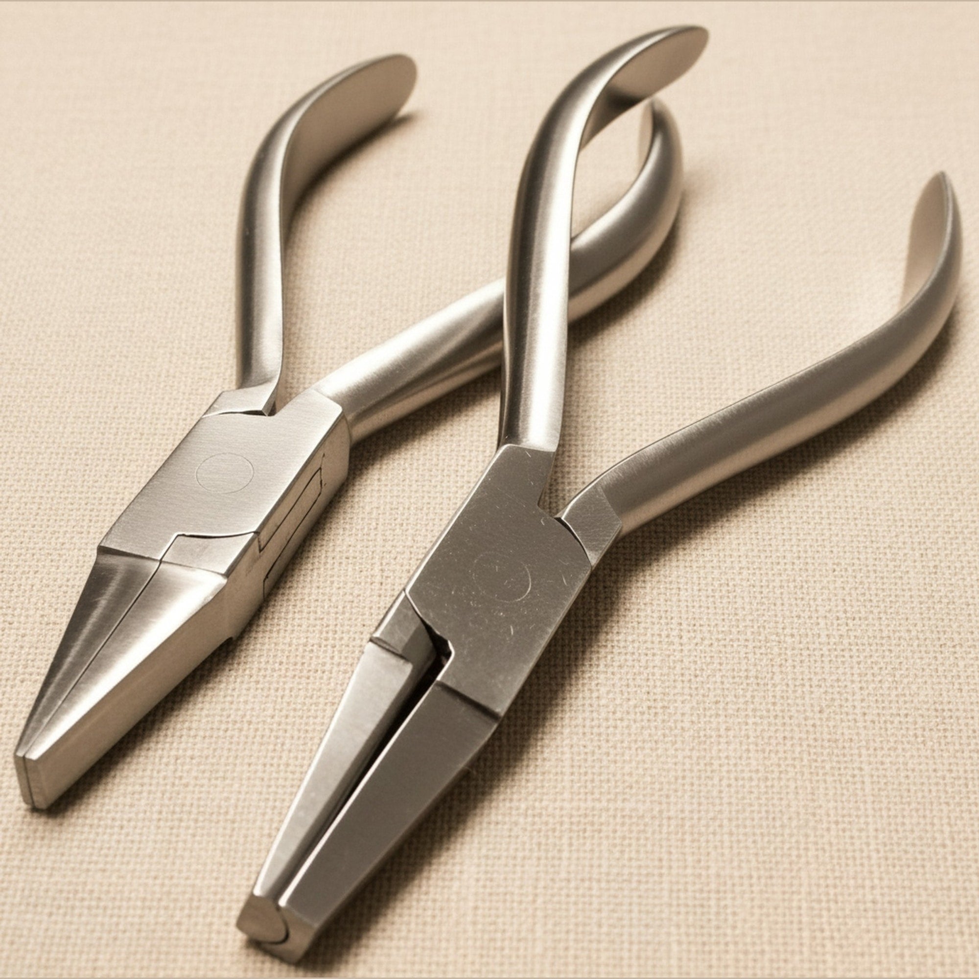 Set of two stainless steel orthodontic pliers, one with flat nose jaws and one with half-round concave jaws, shown side by side.