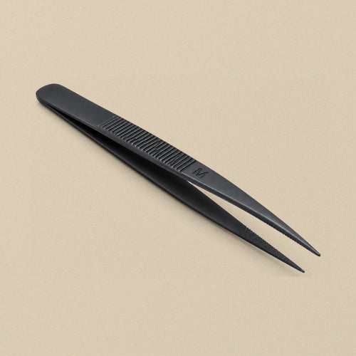 Black anodised diamond tweezers with serrated tips and a ribbed grip stamped 'M', lying on a beige background