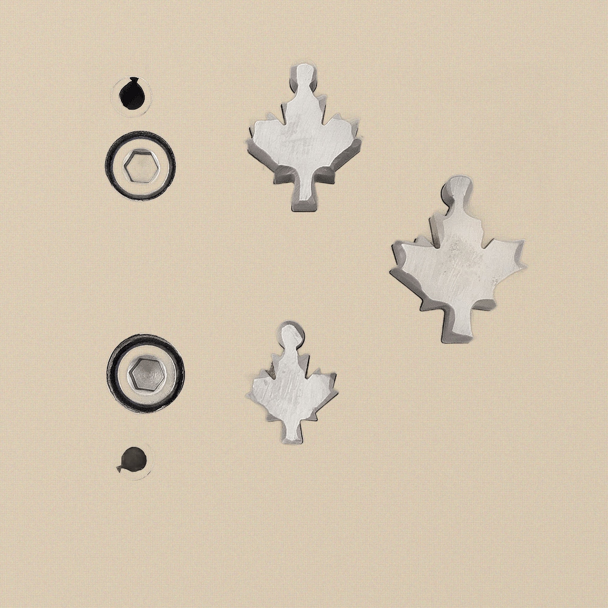 Hardened steel disc cutter block with three maple leaf shaped punches arranged neatly beside it.