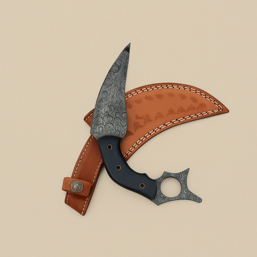 Raindrop Damascus karambit knife laid across its tooled tan leather sheath, finger ring at the end of the handle