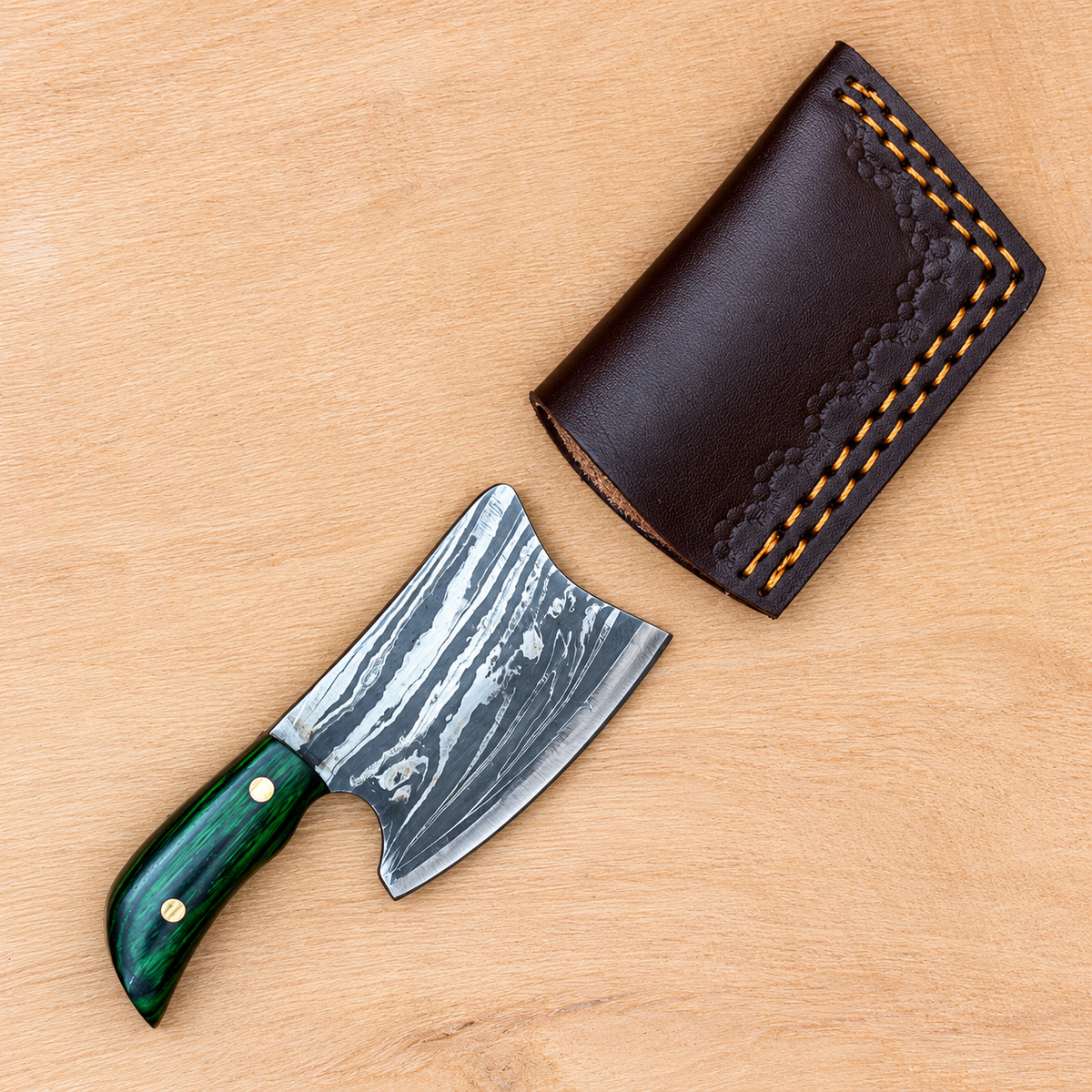 Miniature Damascus cleaver knife beside its brown leather sheath on a wooden surface