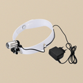 Head-mounted examination lamp on an adjustable white headband, with its plug-in charger