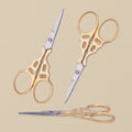 Gold-plated decorative embroidery scissors with ornate handles, shown closed on a white background.