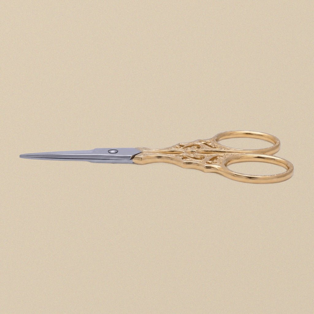 Close-up of the ornate, cut-out handles of the gold-plated embroidery scissors.