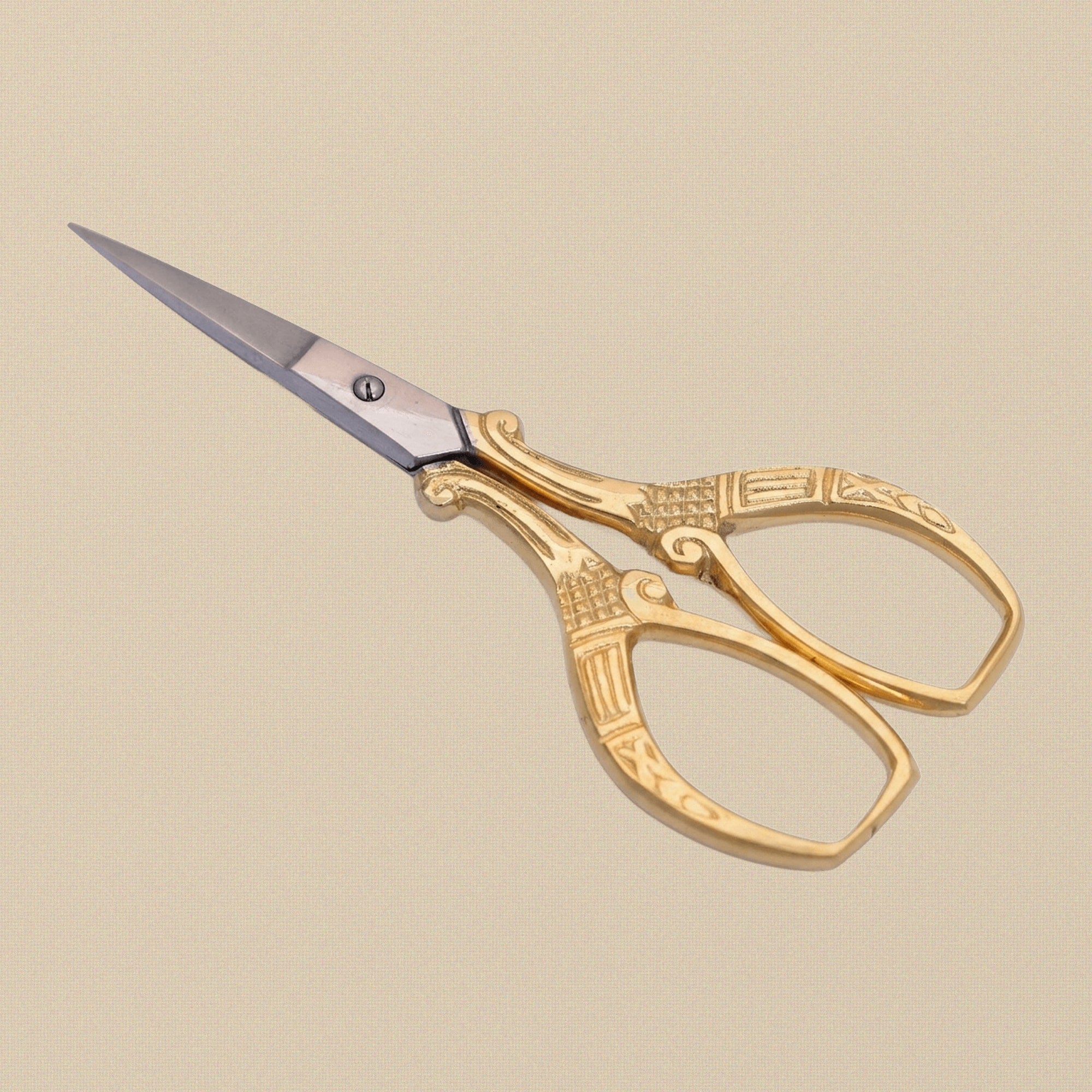 A pair of gold-plated embroidery scissors with ornate scroll-pattern handles, shown closed on a white background.