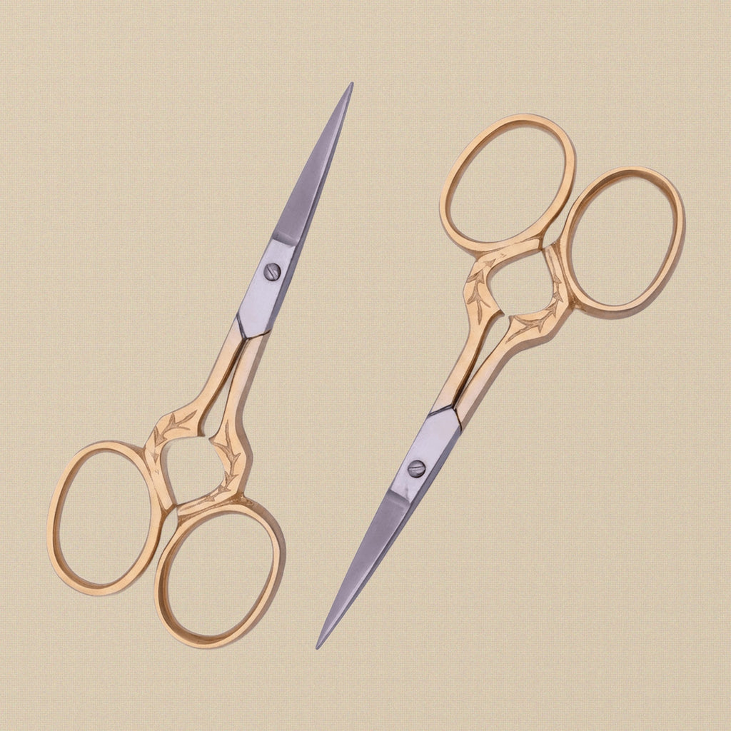 Gold-plated embroidery scissors with leaf-shaped handles, shown closed on a white background.