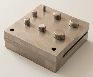 Oval steel disc cutter set, square two-part block with seven oval punches of different sizes standing in it