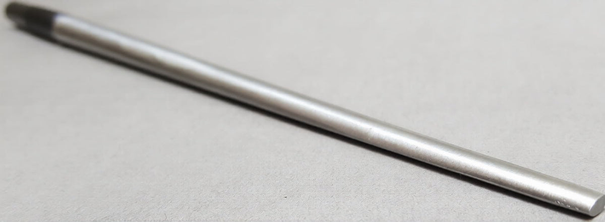 Oval bezel mandrel, long slim tapered steel rod with a darkened end, laid diagonally on a grey surface