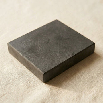 Black square natural test stone, a flat slab with a matt surface, lying on linen